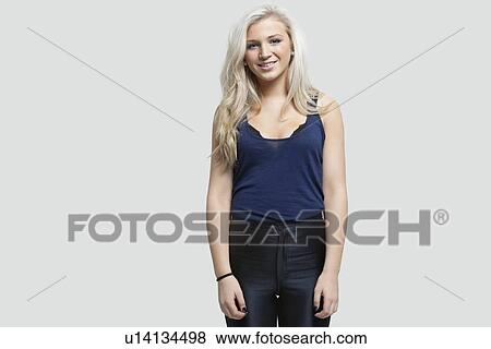 Stock Photo - Portrait of young woman standing against gray background. Fotosearch