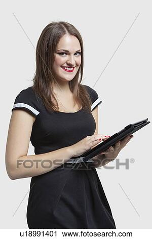 Stock Image - Portrait of young woman using tablet PC over gray background. Fotosearch