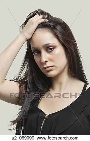 Portrait of young woman with hand in hair against gray background View Large Photo Image Stock Image - Portrait of young woman with hand in hair against gray background. Fotosearch