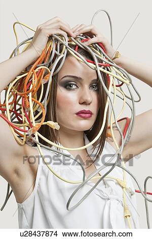 Picture - Portrait of young woman with head tangled in colorful cables over gray background. Fotosearch