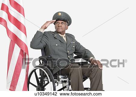 Stock Image - Senior male US military officer in wheelchair saluting American flag over gray background. Fotosearch
