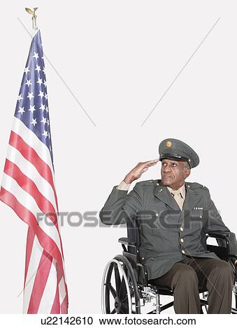 Stock Image - Senior male US military officer in wheelchair saluting American flag over gray background. Fotosearch