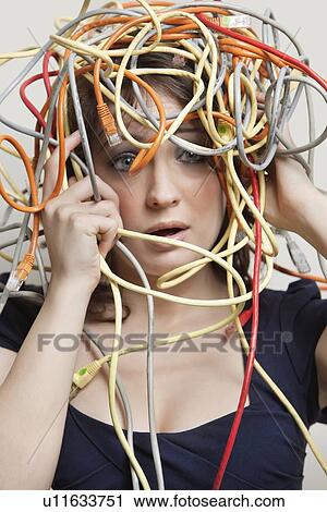 Stock Image - Shocked young woman's head tangled in colorful cables over gray background. Fotosearch