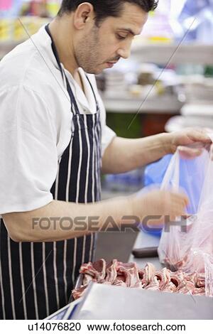 Stock Image - Side view of man working in butcher shop. Fotosearch