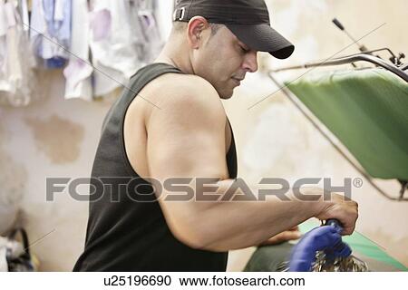 Stock Image - Side view of mature man ironing at laundry. Fotosearch