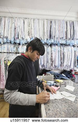 Side view of young man working at dry cleaning shop View Large Photo Image Stock Photo - Side view of young man working at dry cleaning shop. Fotosearch
