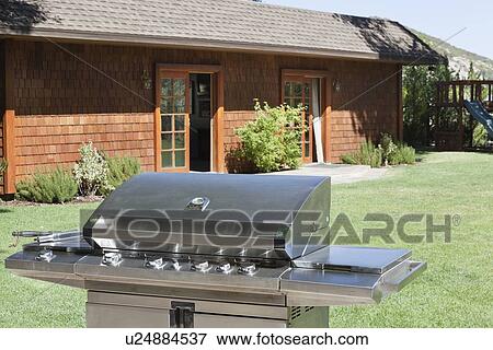 Stock Photo - Stainless steel barbecue grill in front of house at lawn. Fotosearch