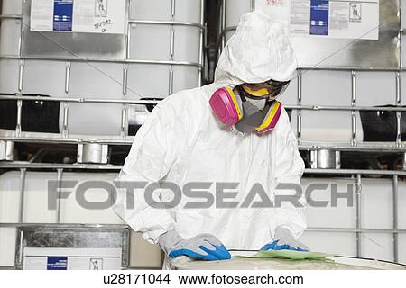 Picture - Technician in hazmat suit reading instructions on paper. Fotosearch