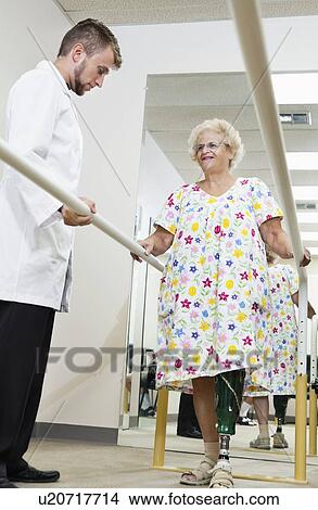 Picture - Technician looking at senior woman having ambulatory therapy. Fotosearch