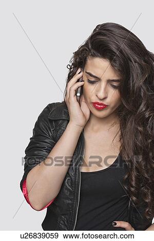 Stock Photo - Thoughtful young woman using cell phone over gray background. Fotosearch