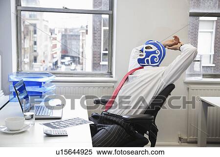 Stock Photography - Tired businessman stretching in wrestling mask at office desk. Fotosearch