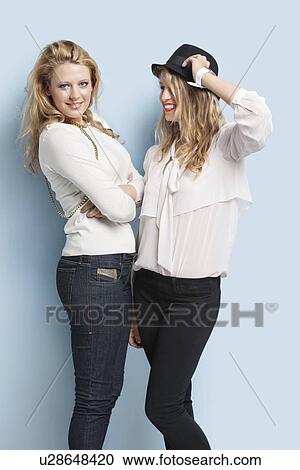 Stock Image - Two happy young women standing together against light blue background. Fotosearch