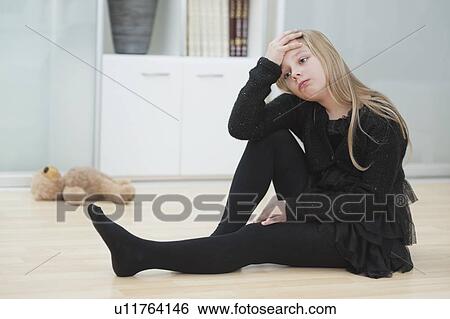 Upset girl with hand on head sits on hardwood floor at home View Large Photo Image Stock Photograph - Upset girl with hand on head sits on hardwood floor at home. Fotosearch