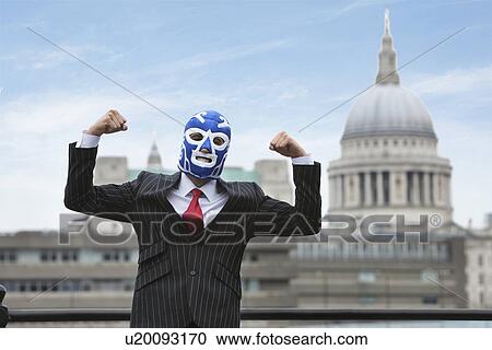 Stock Image - Young businessman flexing muscles in wrestling mask with St. Paul's Cathedral in the background. Fotosearch
