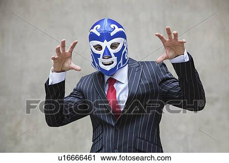 Stock Image - Young businessman gesturing in wrestling mask and pinstripes suit over gray background. Fotosearch