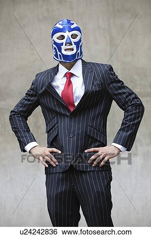 Stock Photograph - Young businessman in pinstripes suit and wrestling mask over gray background. Fotosearch