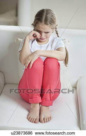 Stock Photograph - Young girl crying while sitting on sofa. Fotosearch