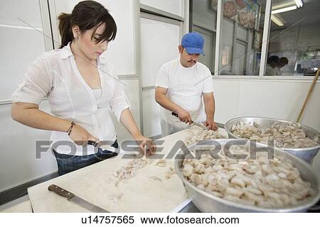 Stock Photography - Young male and female fishmongers cutting prawns. Fotosearch