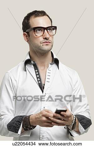 Picture - Young man using cell phone for text messaging against gray background. Fotosearch