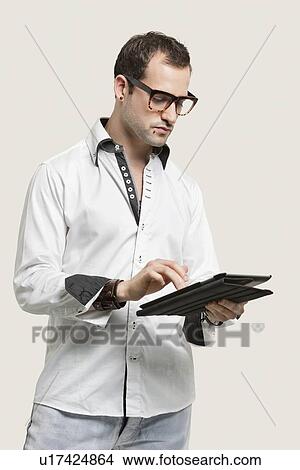 Young man using digital tablet against gray background View Large Photo Image Picture - Young man using digital tablet against gray background. Fotosearch