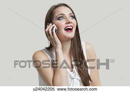 Young woman using cell phone while looking up over gray background View Large Photo Image Stock Photography - Young woman using cell phone while looking up over gray background. Fotosearch