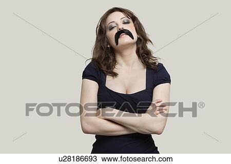 Young woman with arms crossed wearing fake mustache over gray background View Large Photo Image Stock Image - Young woman with arms crossed wearing fake mustache over gray background. Fotosearch