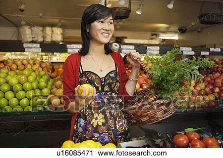 Beautiful young woman holding lemon with basket while looking away in market View Large Photo Image Stock Image - Beautiful young woman holding lemon with basket while looking away in market. Fotosearch
