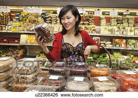 Stock Photograph - Beautiful young woman looking at produce in package in market. Fotosearch