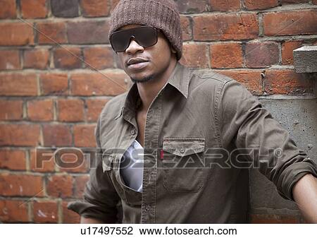 Stock Image - Close-up Portrait of a young African American man standing against brick wall. Fotosearch