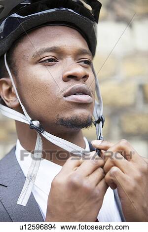 Picture - Close-up portrait of African American businessman putting on bicycle helmet. Fotosearch