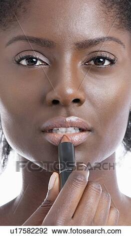 Stock Image - Close-up portrait of young African American woman applying lipstick. Fotosearch