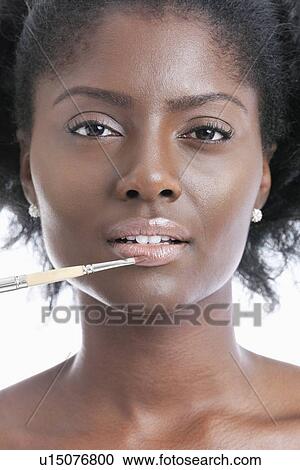 Stock Image - Close-up portrait of young woman applying lip gloss with brush. Fotosearch