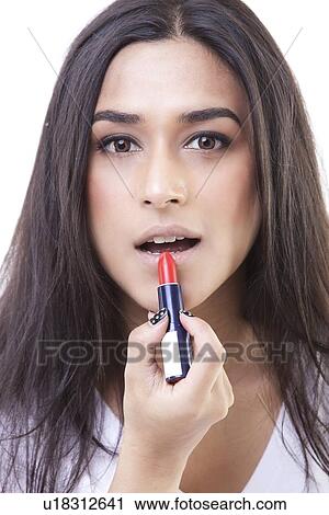 Stock Image - Close-up portrait of young woman applying lipstick over white background. Fotosearch