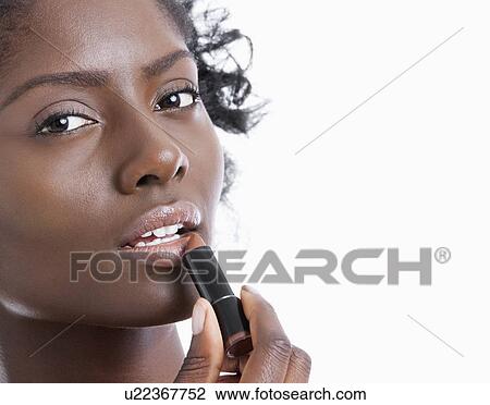 Stock Image - Close-up portrait of young woman applying lipstick over white background. Fotosearch
