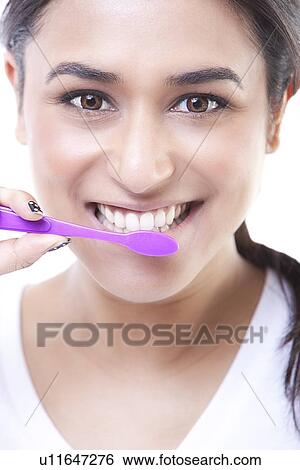 Stock Photograph - Close-up portrait of young woman brushing teeth over white background. Fotosearch