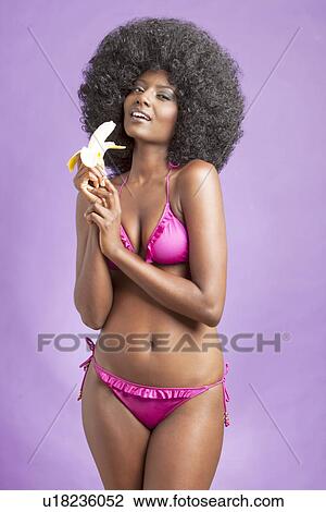 Flirtatious young woman in bikini holding banana against violet background View Large Photo Image Stock Image - Flirtatious young woman in bikini holding banana against violet background. Fotosearch