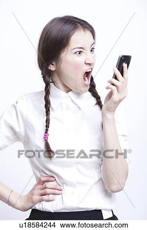 Picture - Furious young woman screaming into her cell phone against white background. Fotosearch