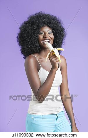 Happy stylish young woman eating banana against violet background View Large Photo Image Stock Image - Happy stylish young woman eating banana against violet background. Fotosearch