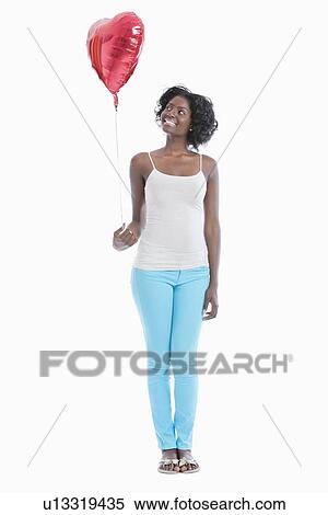 Stock Photography - Happy young woman looking at heart shaped balloon over white background. Fotosearch