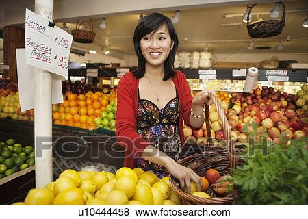 Stock Photo - Happy young woman looking away while selecting lemon. Fotosearch