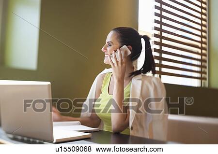 Happy young woman sitting at desk with laptop using cell phone View Large Photo Image Stock Photo - Happy young woman sitting at desk with laptop using cell phone. Fotosearch