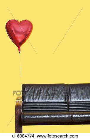 Heart shaped balloon tied to sofa over yellow background View Large Photo Image Picture - Heart shaped balloon tied to sofa over yellow background. Fotosearch