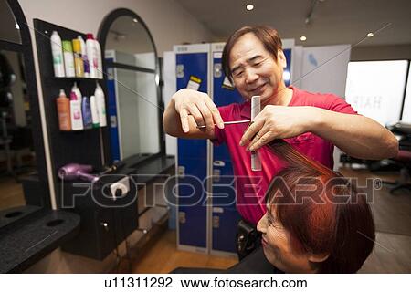 Stock Image - Male Korean Hair Dresser cuts Female customers hair. Fotosearch