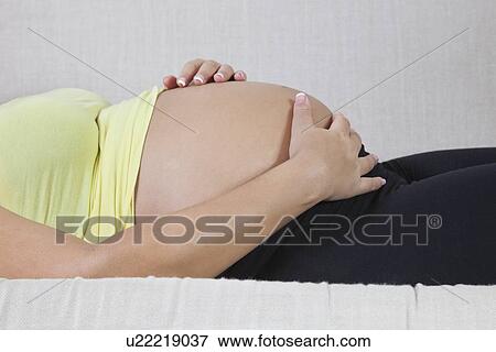 Midsection of young pregnant woman with hands on stomach relaxing at home View Large Photo Image Stock Photo - Midsection of young pregnant woman with hands on stomach relaxing at home. Fotosearch