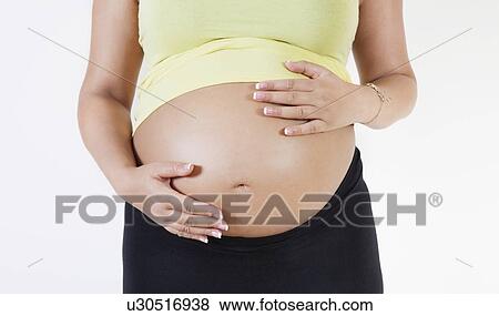 Midsection of young pregnant woman with hands on stomach against white background View Large Photo Image Stock Photo - Midsection of young pregnant woman with hands on stomach against white background. Fotosearch