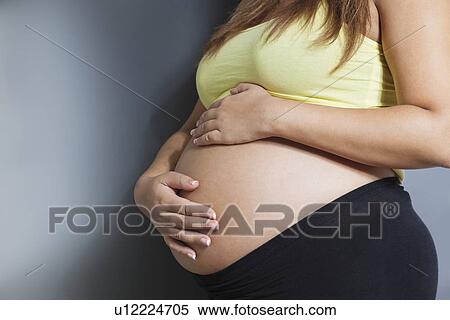Midsection of young pregnant woman with hands on stomach against gray background View Large Photo Image Stock Photography - Midsection of young pregnant woman with hands on stomach against gray background. Fotosearch