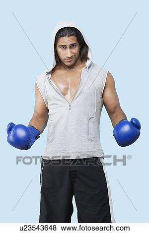 Portrait of a confident young man wearing boxing gloves standing over blue background View Large Photo Image Stock Photo - Portrait of a confident young man wearing boxing gloves standing over blue background. Fotosearch