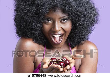 Stock Photo - Portrait of a flirtatious young woman with fizzy hair holding cherries. Fotosearch