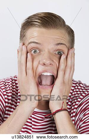 Portrait of a shocked young man with hands on face over white background View Large Photo Image Stock Image - Portrait of a shocked young man with hands on face over white background. Fotosearch
