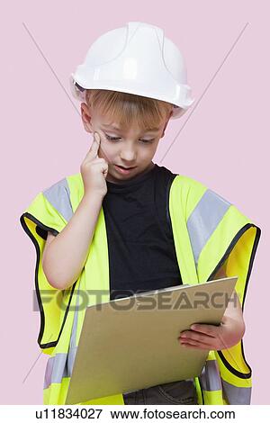 Portrait of a thoughtful young boy dressed as construction worker looking at clipboard over pink background View Large Photo Image Stock Photo - Portrait of a thoughtful young boy dressed as construction worker looking at clipboard over pink background. Fotosearch